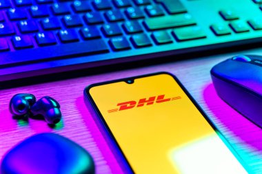 Prag, Çek Cumhuriyeti - 08 12 2025: DHL logosunu gösteren klavyesi ve cep telefonu olan bir masanın yan görüntüsü. DHL uluslararası nakliye hizmeti sunan bir lojistik şirketidir..
