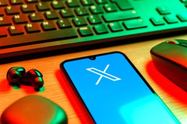 Prague, Czechia - 08 12 2025: A side view of a desk with a keyboard and a mobile phone displaying the X logo. X is a platform for sharing short posts and updates.