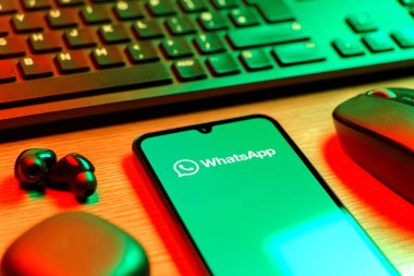 Prague, Czechia - 08 12 2025: A side view of a desk with a keyboard and a mobile phone displaying the WhatsApp logo. WhatsApp is an app for sending texts, calls, and media.