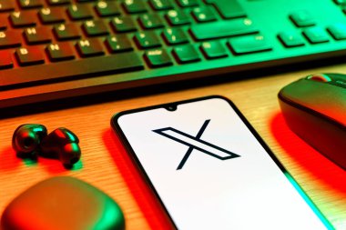 Prague, Czechia - 08 12 2025: A side view of a desk with a keyboard and a mobile phone displaying the X logo. X is a platform for sharing short posts and updates.