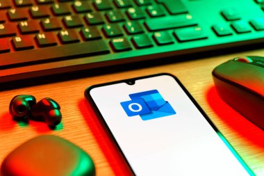 Prague, Czechia - 08 12 2025: A side view of a desk with a keyboard and a mobile phone displaying the Outlook logo. Outlook is an email platform for sending and managing messages.