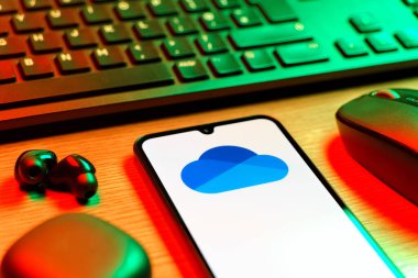 Prague, Czechia - 08 12 2025: A side view of a desk with a keyboard and a mobile phone displaying the OneDrive logo. OneDrive is a cloud storage platform for saving and sharing files.