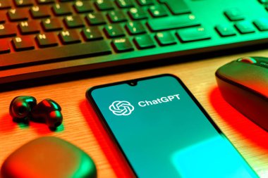 Prague, Czechia - 08 12 2025: A side view of a desk with a keyboard and a mobile phone displaying the ChatGPT logo. ChatGPT is an AI chatbot for generating text and answering questions.