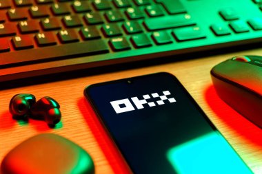 Prague, Czechia - 08 12 2025: A side view of a desk with a keyboard and a mobile phone displaying the OKX logo. OKX is a cryptocurrency exchange for trading digital assets.