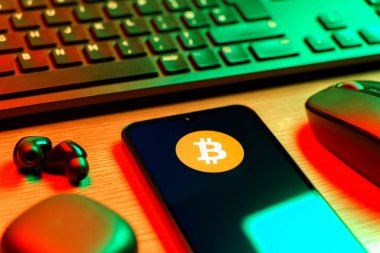Prag, Çek Cumhuriyeti - 08 12 2025: Bitcoin logosunu gösteren klavyesi ve cep telefonu olan bir masanın yan görüntüsü. Bitcoin merkezi olmayan işlemler için dijital bir kripto para birimidir.
