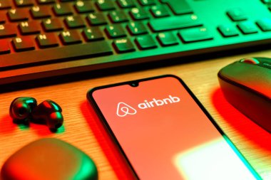 Prag, Çek Cumhuriyeti - 08 12 2025: Airbnb logosunu gösteren klavyesi ve cep telefonu olan bir masanın yan görüntüsü. Airbnb dünya çapında kısa vadeli konaklama için bir platformdur..