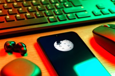 Prag, Çek Cumhuriyeti - 08 12 2025: Vikipedi logosunu gösteren klavyesi ve cep telefonu olan bir masanın yan görüntüsü. Vikipedi çevrimiçi bir ansiklopedidir..