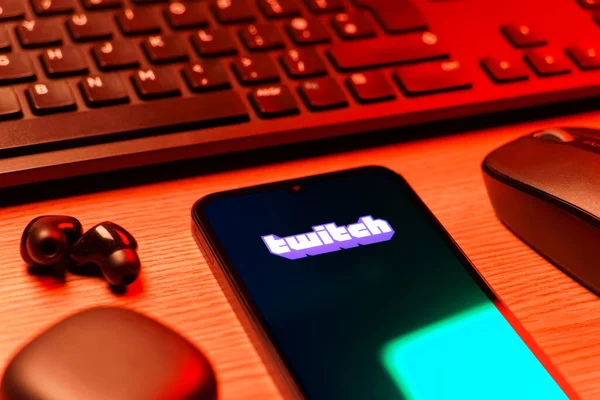 Prague, Czechia - 08 12 2025: A side view of a desk with a keyboard and a mobile phone displaying the Twitch logo. Twitch is a platform for live streaming games and content.