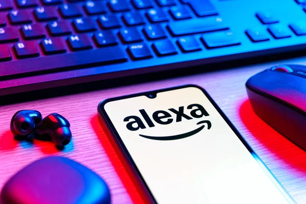 Prag, Çek Cumhuriyeti - 08 12 2025: Alexa logosunu gösteren klavyesi ve cep telefonu olan bir masanın yan görüntüsü. Alexa akıllı aygıtlar ve servisler için ses asistanıdır.