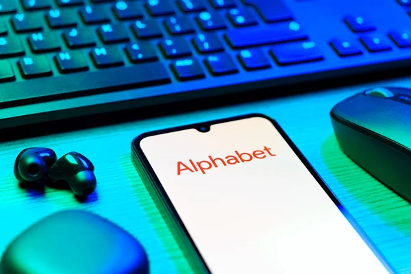 Prague, Czechia - 08 12 2025: A side view of a desk with a keyboard and a mobile phone displaying the Alphabet logo. Alphabet is a parent company of Google and other tech ventures.