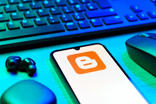 Prag, Çek Cumhuriyeti - 08 12 2025: Blogger logosunu gösteren klavyesi ve cep telefonu olan bir masanın yan görüntüsü. Blogger blog oluşturma ve yayınlama için bir platformdur.