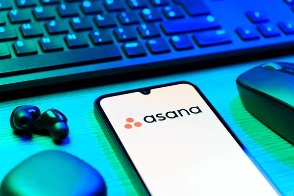 Prag, Çek Cumhuriyeti - 08 12 2025: Asana logosunu gösteren klavyesi ve cep telefonu olan bir masanın yan görüntüsü. Asana görev yönetimi ve takım işbirliği için bir platformdur..