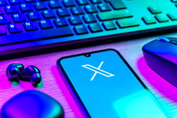 Prague, Czechia - 08 12 2025: A side view of a desk with a keyboard and a mobile phone displaying the X logo. X is a platform for sharing short posts and updates.