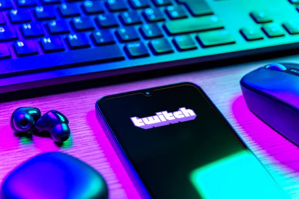Prague, Czechia - 08 12 2025: A side view of a desk with a keyboard and a mobile phone displaying the Twitch logo. Twitch is a platform for live streaming games and content.