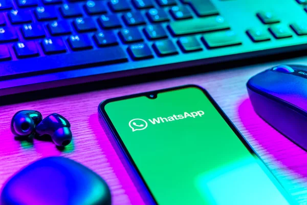 Prague, Czechia - 08 12 2025: A side view of a desk with a keyboard and a mobile phone displaying the WhatsApp logo. WhatsApp is an app for sending texts, calls, and media.