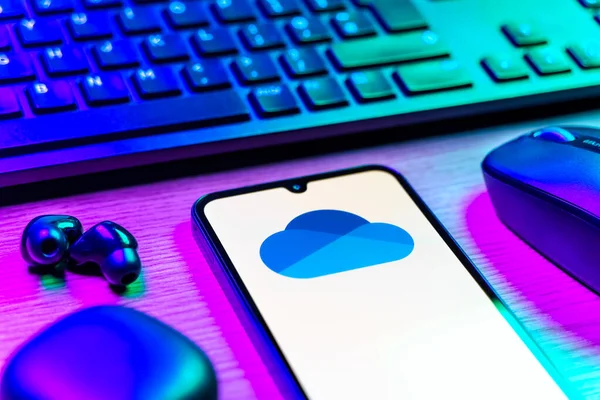 Prague, Czechia - 08 12 2025: A side view of a desk with a keyboard and a mobile phone displaying the OneDrive logo. OneDrive is a cloud storage platform for saving and sharing files.