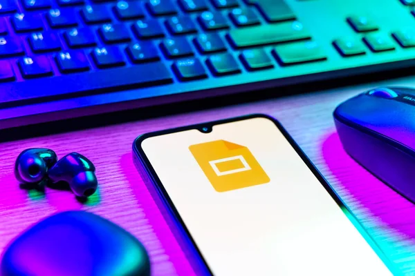 Prag, Çek Cumhuriyeti - 08 12 2025: Google Slides logosunu gösteren klavyesi ve cep telefonu olan bir masanın yan görüntüsü. Google Slides sunumlar ve slayt gösterileri oluşturmak için bir platformdur.