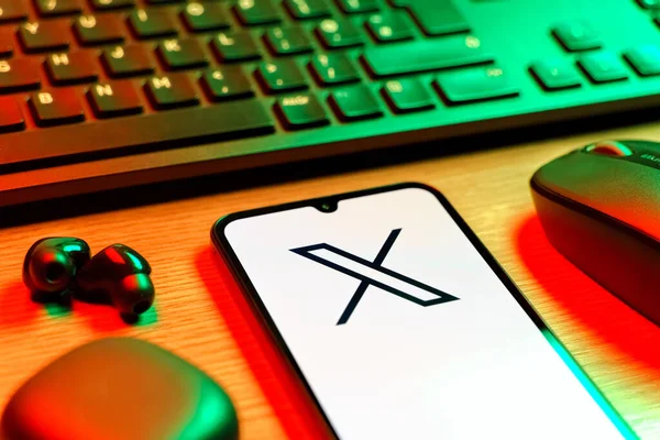 Prague, Czechia - 08 12 2025: A side view of a desk with a keyboard and a mobile phone displaying the X logo. X is a platform for sharing short posts and updates.