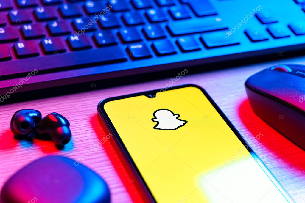 Prague, Czechia - 08 12 2025: A side view of a desk with a keyboard and a mobile phone displaying the Snapchat logo. Snapchat is an app for sending photos, videos, and temporary messages.