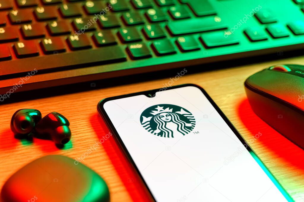 Prague, Czechia - 08 12 2025: A side view of a desk with a keyboard and a mobile phone displaying the Starbucks logo. Starbucks is a global coffeehouse chain serving beverages and food.