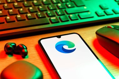 Prag, Çek Cumhuriyeti - 08 12 2025: Kenar logosunu gösteren klavyesi ve cep telefonu olan bir masanın yan görüntüsü. Edge, Microsoft tarafından Windows aygıtları için geliştirilen bir web tarayıcısıdır..