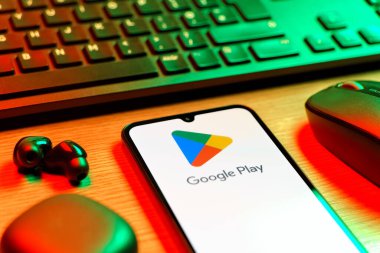 Prag, Çek Cumhuriyeti - 08 12 2025: Google Play logosunu gösteren klavyesi ve cep telefonu olan bir masanın yan görüntüsü. Google Play uygulamaları, oyunları ve dijital içeriği indirmek için bir platformdur.