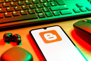 Prag, Çek Cumhuriyeti - 08 12 2025: Blogger logosunu gösteren klavyesi ve cep telefonu olan bir masanın yan görüntüsü. Blogger blog oluşturma ve yayınlama için bir platformdur.
