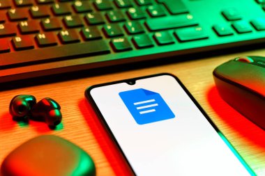 Prag, Çek Cumhuriyeti - 08 12 2025: Google Docs logosunu gösteren klavyesi ve cep telefonu olan bir masanın yan görüntüsü. Google Docs metin belgeleri oluşturmak ve düzenlemek için bir platformdur.
