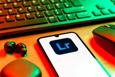 Prag, Çek Cumhuriyeti - 08 12 2025: Lightroom logosunu gösteren klavyesi ve cep telefonu olan bir masanın yan görüntüsü. Lightroom fotoğraf düzenleme ve yönetim için bir yazılımdır..