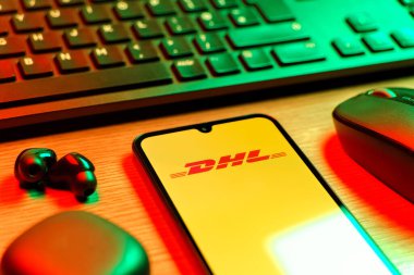Prag, Çek Cumhuriyeti - 08 12 2025: DHL logosunu gösteren klavyesi ve cep telefonu olan bir masanın yan görüntüsü. DHL uluslararası nakliye hizmeti sunan bir lojistik şirketidir..