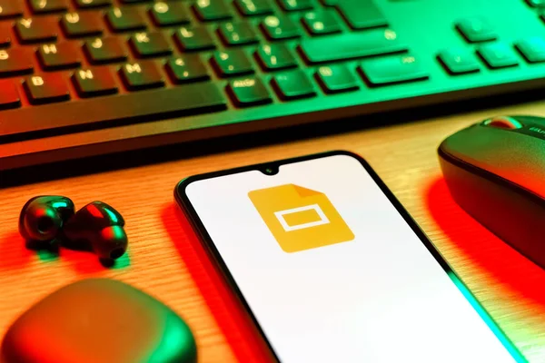 Prag, Çek Cumhuriyeti - 08 12 2025: Google Slides logosunu gösteren klavyesi ve cep telefonu olan bir masanın yan görüntüsü. Google Slides sunumlar ve slayt gösterileri oluşturmak için bir platformdur.