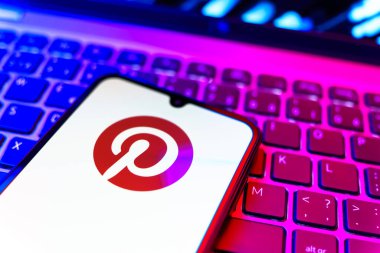 Prag, Çek Cumhuriyeti - 08 19 2025: Pinterest logosunu gösteren klavyenin üzerinde duran cep telefonunun yakından görüntüsü. Pinterest fikirleri görsel olarak keşfetmek ve kaydetmek için bir platformdur..