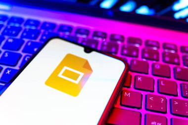Prag, Çek Cumhuriyeti - 08 19 2025: Google Slides logosunu gösteren klavyenin üzerinde duran cep telefonunun yakından görüntüsü. Google Slides sunumlar ve slayt gösterileri oluşturmak için bir platformdur.