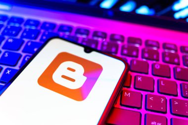 Prag, Çek Cumhuriyeti - 08 19 2025: Klavyenin üzerinde duran ve Blogger logosunu gösteren cep telefonunun yakından görüntüsü. Blogger blog oluşturma ve yayınlama için bir platformdur.