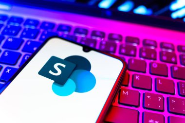 Prag, Çek Cumhuriyeti - 08 19 2025: Microsoft Sharepoint logosunu gösteren klavyenin üzerinde duran cep telefonunun yakından görüntüsü. Microsoft Sharepoint işbirliği ve belge yönetimi için bir platformdur.