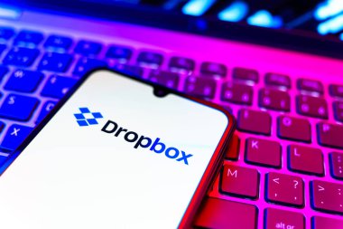Prag, Çek Cumhuriyeti - 08 19 2025: Dropbox logosunu gösteren klavyenin üzerinde duran cep telefonunun yakından görüntüsü. Dropbox bulut depolama ve dosya paylaşımı için bir platformdur.