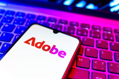 Prag, Çek Cumhuriyeti - 08 19 2025: Klavyede duran ve Adobe logosunu gösteren bir cep telefonunun yakından görüntüsü. Adobe yaratıcı araçlar ve hizmetler sunan bir yazılım şirketidir..