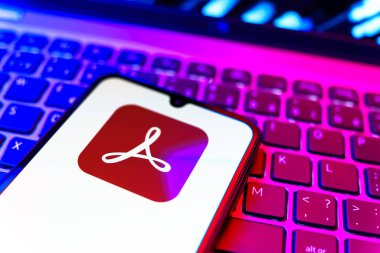 Prag, Çek Cumhuriyeti - 08 19 2025: Klavyede duran ve Akrobat Reader logosunu gösteren cep telefonunun yakından görüntüsü. Acrobat Reader, PDF belgelerini görüntülemek ve yönetmek için bir platformdur.