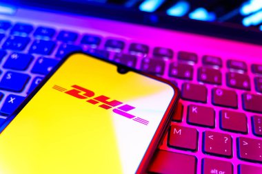 Prag, Çek Cumhuriyeti - 08 19 2025: DHL logosunu gösteren klavyenin üzerinde duran cep telefonunun yakından görüntüsü. DHL uluslararası nakliye hizmeti sunan bir lojistik şirketidir..