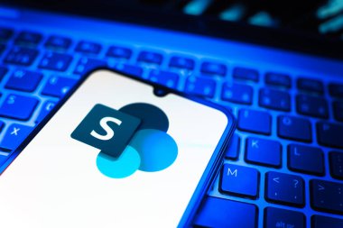 Prag, Çek Cumhuriyeti - 08 19 2025: Microsoft Sharepoint logosunu gösteren klavyenin üzerinde duran cep telefonunun yakından görüntüsü. Microsoft Sharepoint işbirliği ve belge yönetimi için bir platformdur.
