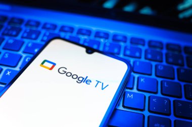 Prag, Çek Cumhuriyeti - 08 19 2025: Google TV logosunu gösteren klavyenin üzerinde duran bir cep telefonunun yakından görüntüsü. Google TV film, program ve uygulamalar için bir platformdur..