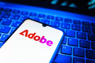 Prag, Çek Cumhuriyeti - 08 19 2025: Klavyede duran ve Adobe logosunu gösteren bir cep telefonunun yakından görüntüsü. Adobe yaratıcı araçlar ve hizmetler sunan bir yazılım şirketidir..