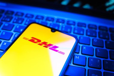 Prag, Çek Cumhuriyeti - 08 19 2025: DHL logosunu gösteren klavyenin üzerinde duran cep telefonunun yakından görüntüsü. DHL uluslararası nakliye hizmeti sunan bir lojistik şirketidir..