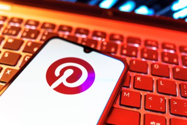 Prag, Çek Cumhuriyeti - 08 19 2025: Pinterest logosunu gösteren klavyenin üzerinde duran cep telefonunun yakından görüntüsü. Pinterest fikirleri görsel olarak keşfetmek ve kaydetmek için bir platformdur..