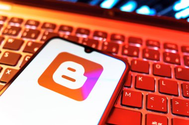 Prag, Çek Cumhuriyeti - 08 19 2025: Klavyenin üzerinde duran ve Blogger logosunu gösteren cep telefonunun yakından görüntüsü. Blogger blog oluşturma ve yayınlama için bir platformdur.