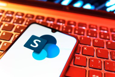 Prag, Çek Cumhuriyeti - 08 19 2025: Microsoft Sharepoint logosunu gösteren klavyenin üzerinde duran cep telefonunun yakından görüntüsü. Microsoft Sharepoint işbirliği ve belge yönetimi için bir platformdur.