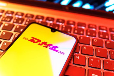 Prag, Çek Cumhuriyeti - 08 19 2025: DHL logosunu gösteren klavyenin üzerinde duran cep telefonunun yakından görüntüsü. DHL uluslararası nakliye hizmeti sunan bir lojistik şirketidir..