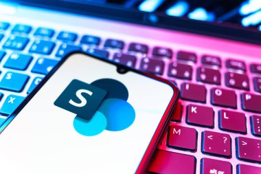 Prag, Çek Cumhuriyeti - 08 19 2025: Microsoft Sharepoint logosunu gösteren klavyenin üzerinde duran cep telefonunun yakından görüntüsü. Microsoft Sharepoint işbirliği ve belge yönetimi için bir platformdur.