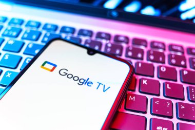 Prag, Çek Cumhuriyeti - 08 19 2025: Google TV logosunu gösteren klavyenin üzerinde duran bir cep telefonunun yakından görüntüsü. Google TV film, program ve uygulamalar için bir platformdur..