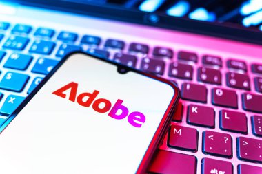 Prag, Çek Cumhuriyeti - 08 19 2025: Klavyede duran ve Adobe logosunu gösteren bir cep telefonunun yakından görüntüsü. Adobe yaratıcı araçlar ve hizmetler sunan bir yazılım şirketidir..